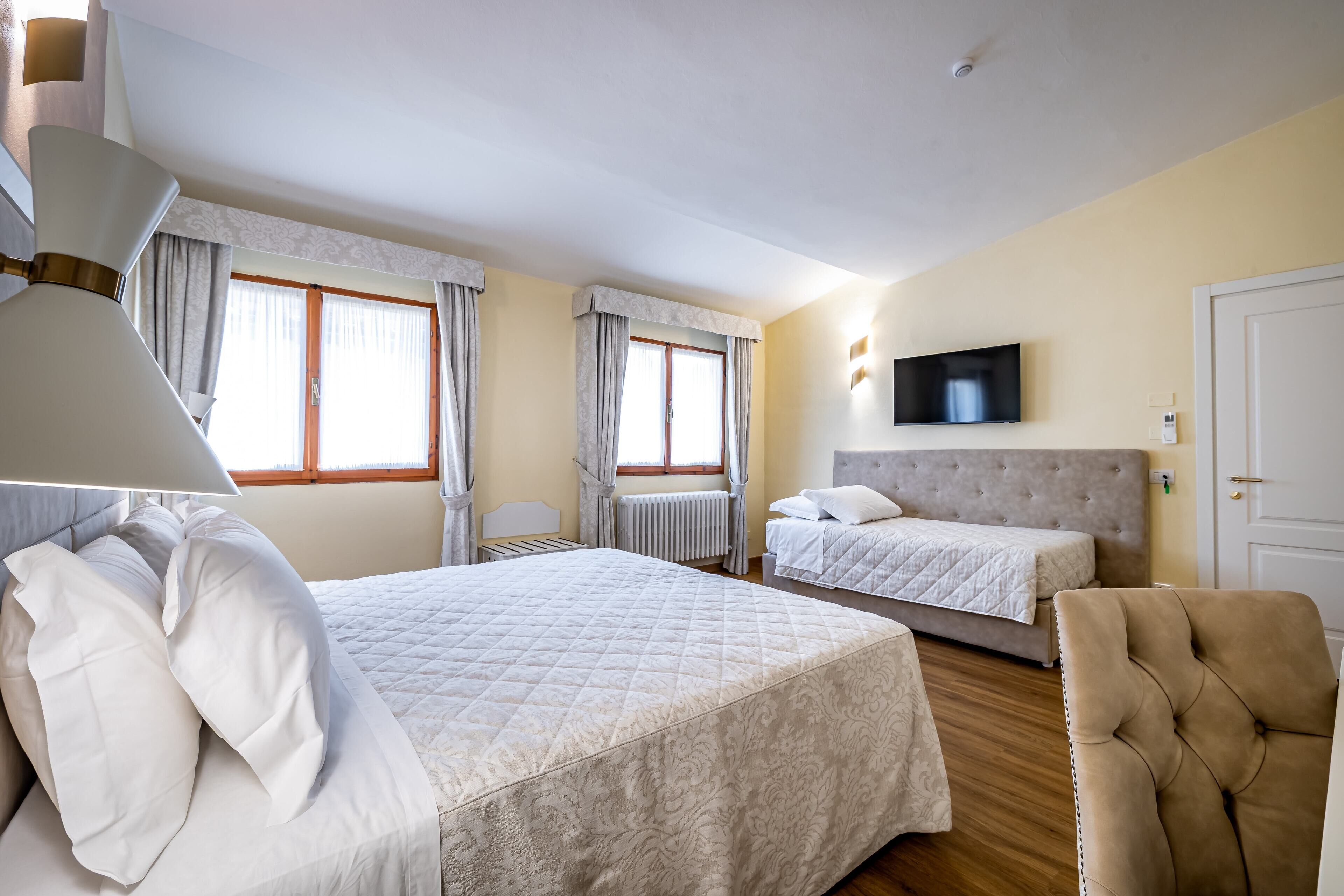 A hotel room with a large bed, a smaller bed, a chair, a TV, and a window with curtains.
