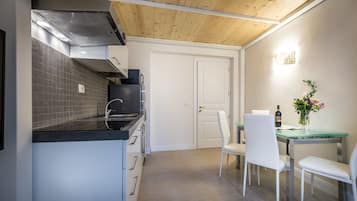 Una cocina moderna con una campana extractora de acero inoxidable, un refrigerador negro y una mesa de comedor con cubierta de vidrio y sillas blancas.