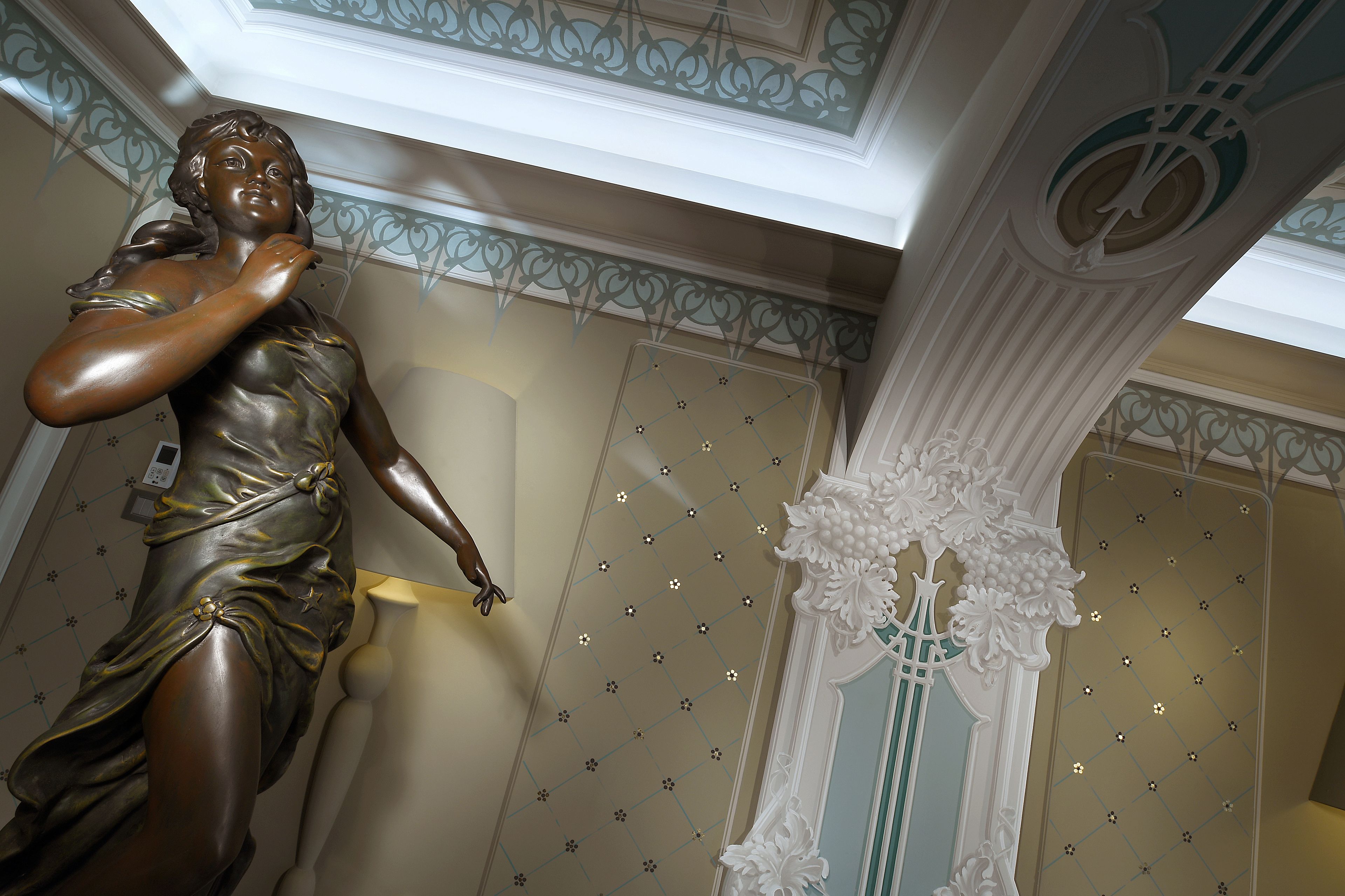 Una estatua de una mujer vestida, un techo decorativo con un diseño geométrico y una columna con relieves florales.