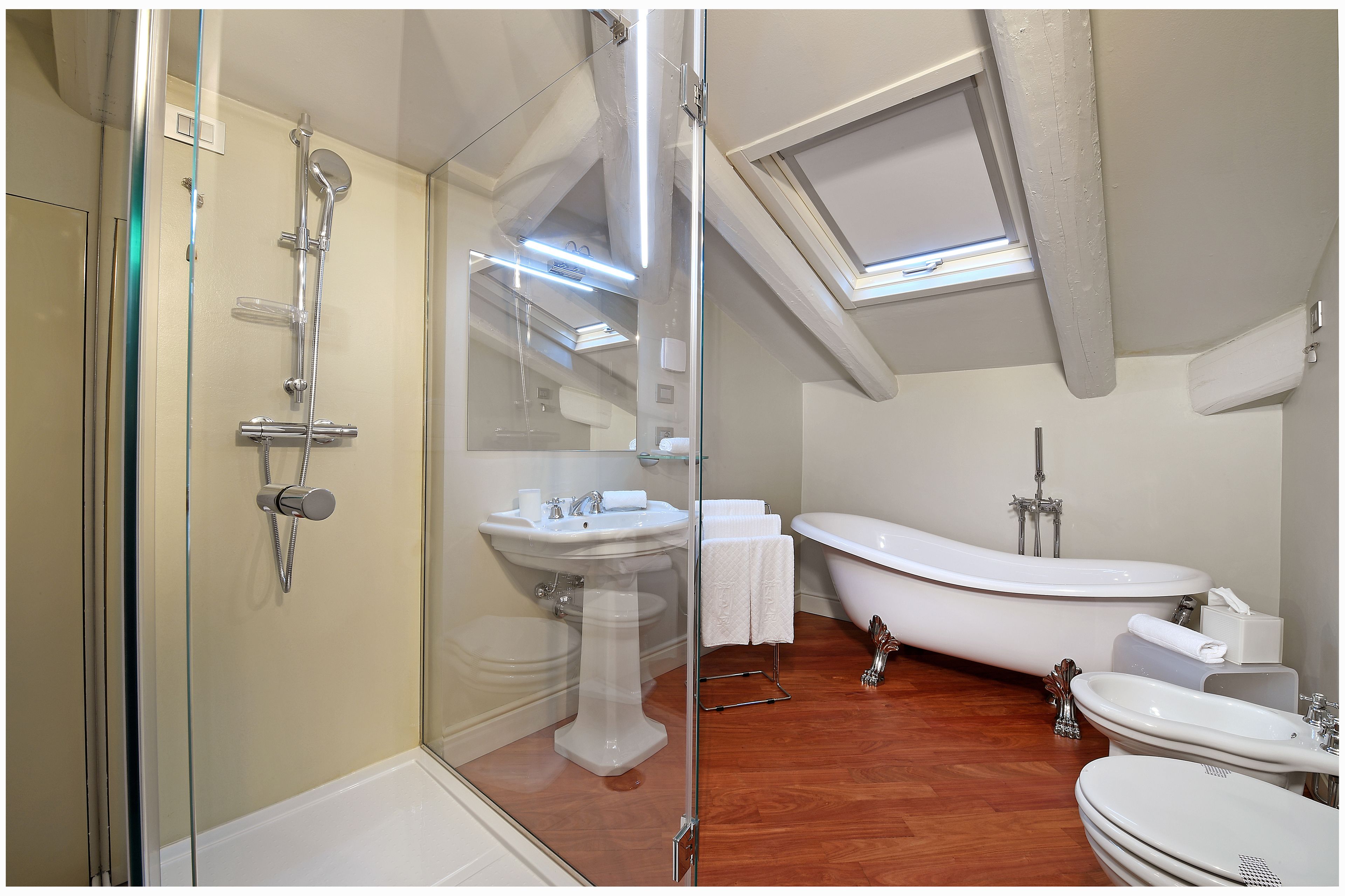 A modern bathroom with a glass-enclosed shower, a pedestal sink, a freestanding bathtub, and a separate vanity with a sink.
