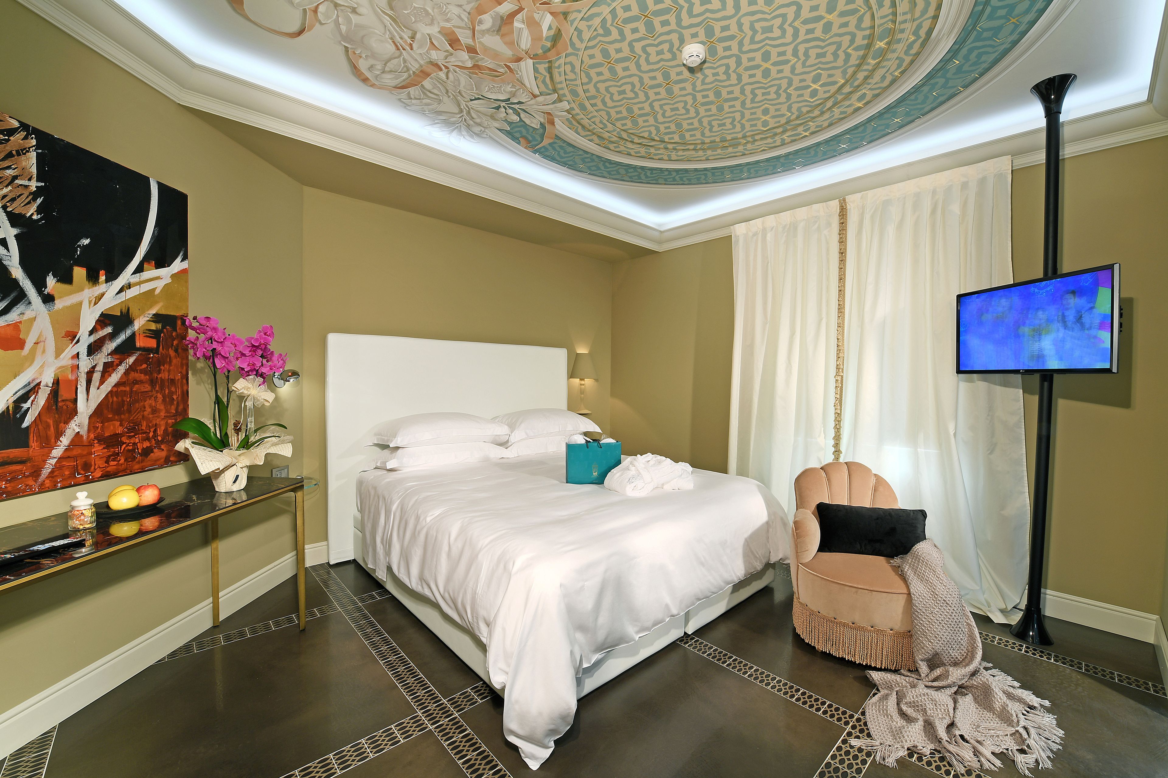 Ein modernes Hotelzimmer mit einem großen Bett, einem Fernseher, einer dekorativen Decke und einem Nachttisch mit Blumen.
