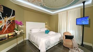 A modern hotel room with a large bed, a TV, a decorative ceiling, and a nightstand with a vase of flowers.