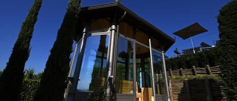 A gazebo with a glass enclosure, surrounded by tall trees and a wooden fence.