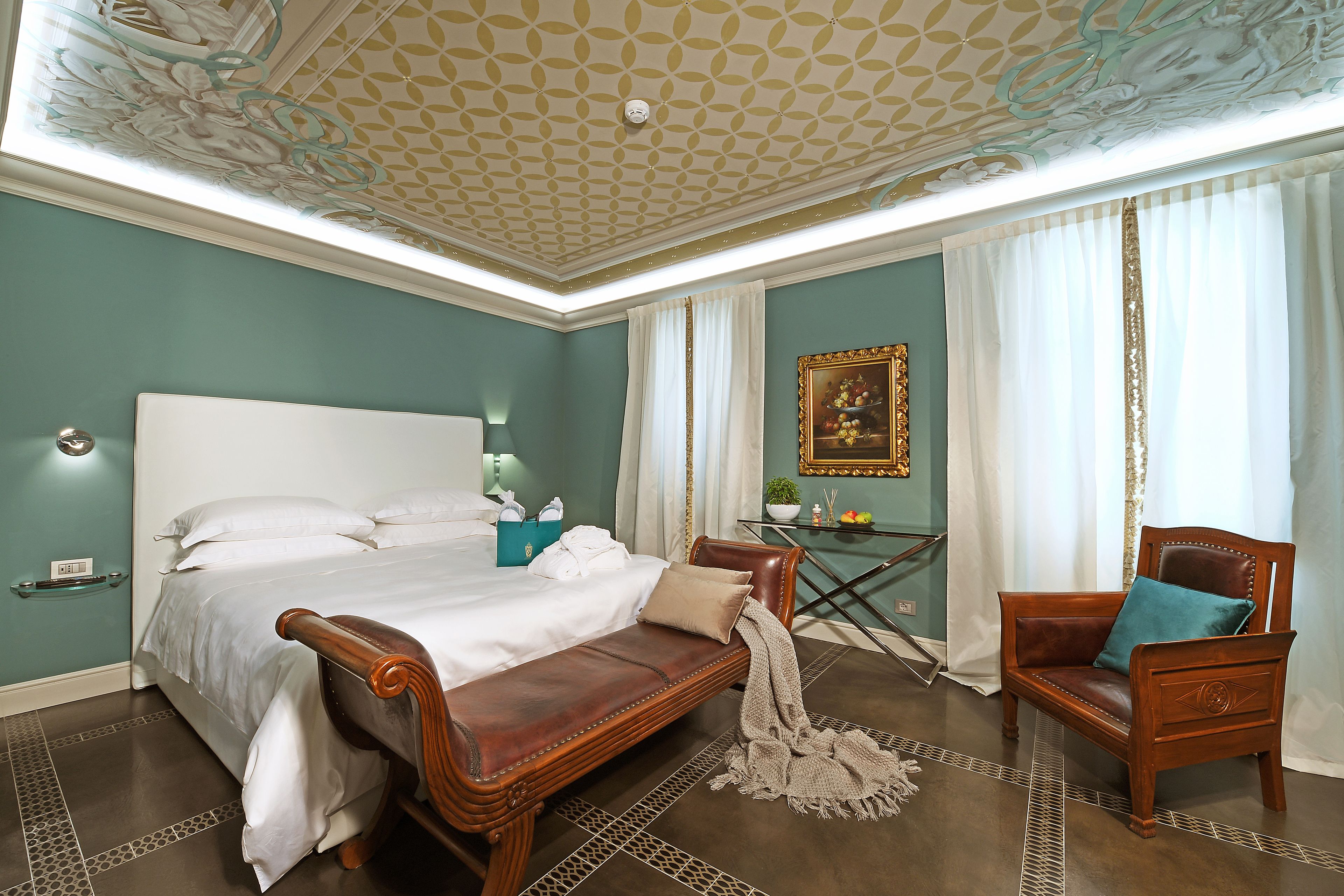 A bedroom with a large bed, a wooden bench, a chair, and a small table with a plant.