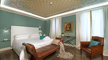 A bedroom with a large bed, a wooden bench, a chair, and a small table with a plant.