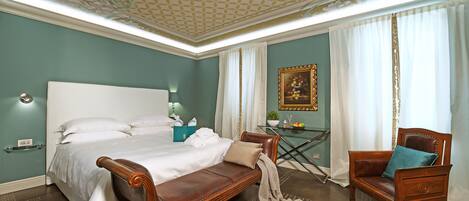 A bedroom with a large bed, a wooden bench, a chair, and a small table with a plant.