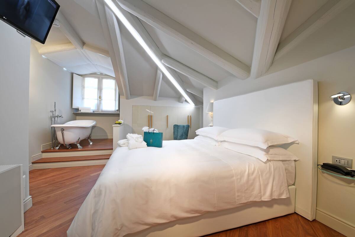 A hotel room with a large bed, a sitting area with a chair, a bathtub, and a television.
