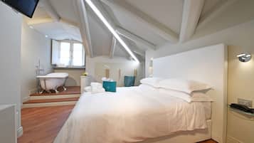 A hotel room with a large bed, a sitting area with a chair, a bathtub, and a television.
