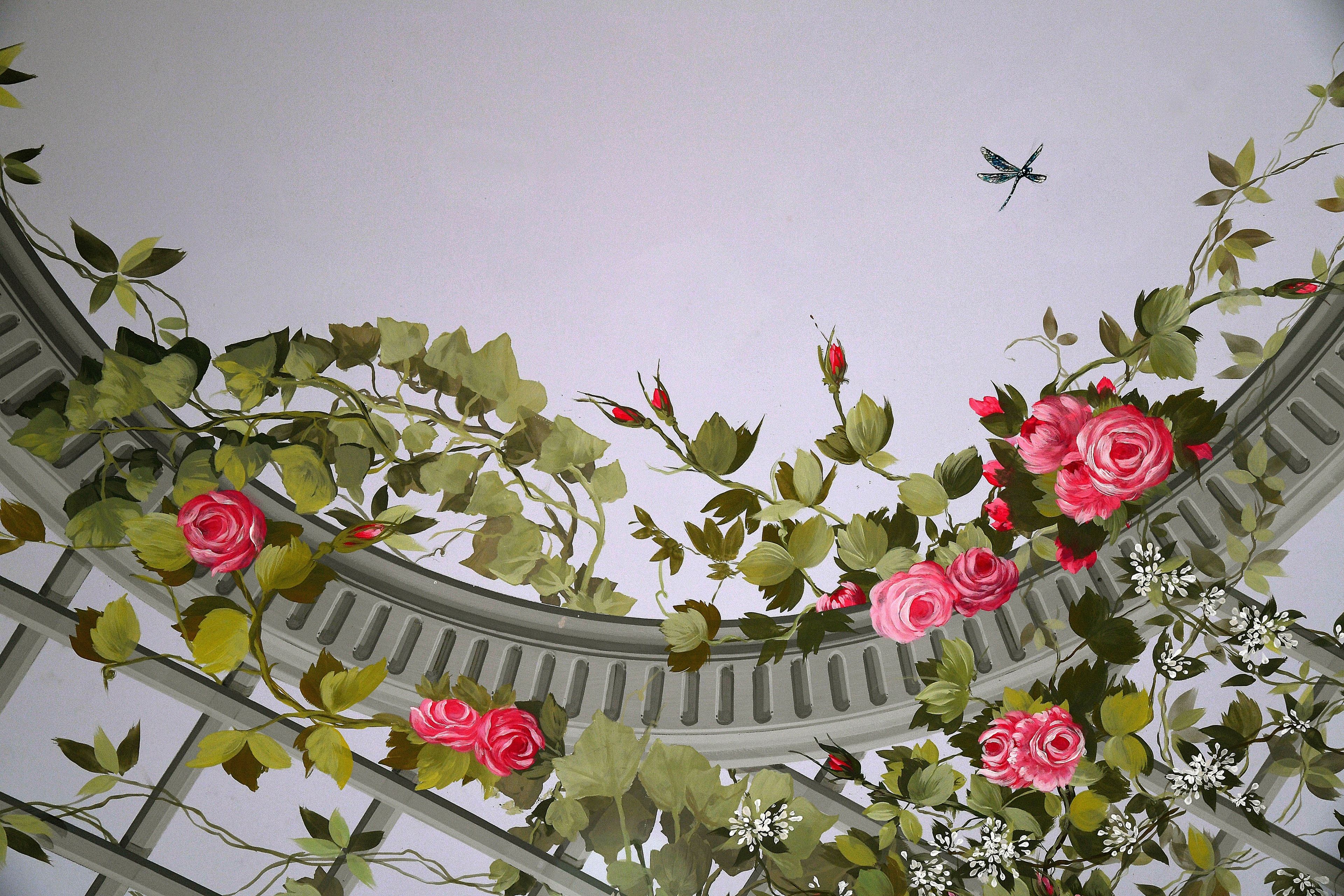A ceiling with a circular design, featuring green foliage and pink flowers.