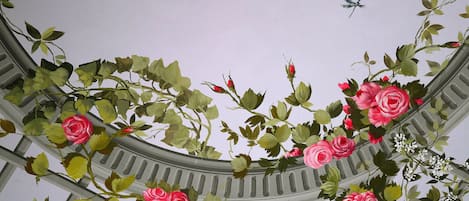 A ceiling with a circular design, featuring green foliage and pink flowers.