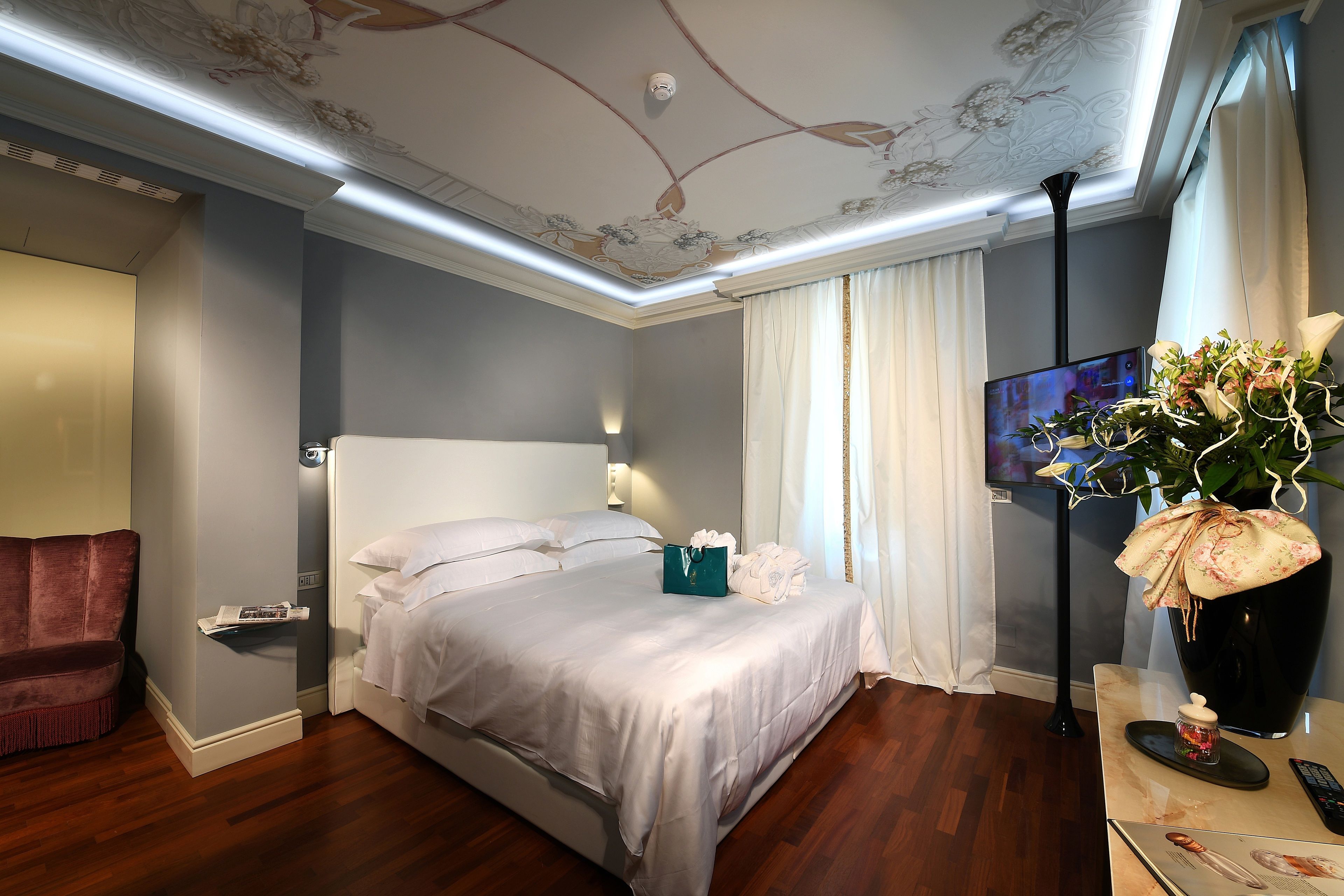A modern hotel room with a large bed, a flat-screen TV, a vase of flowers, and a wooden floor.