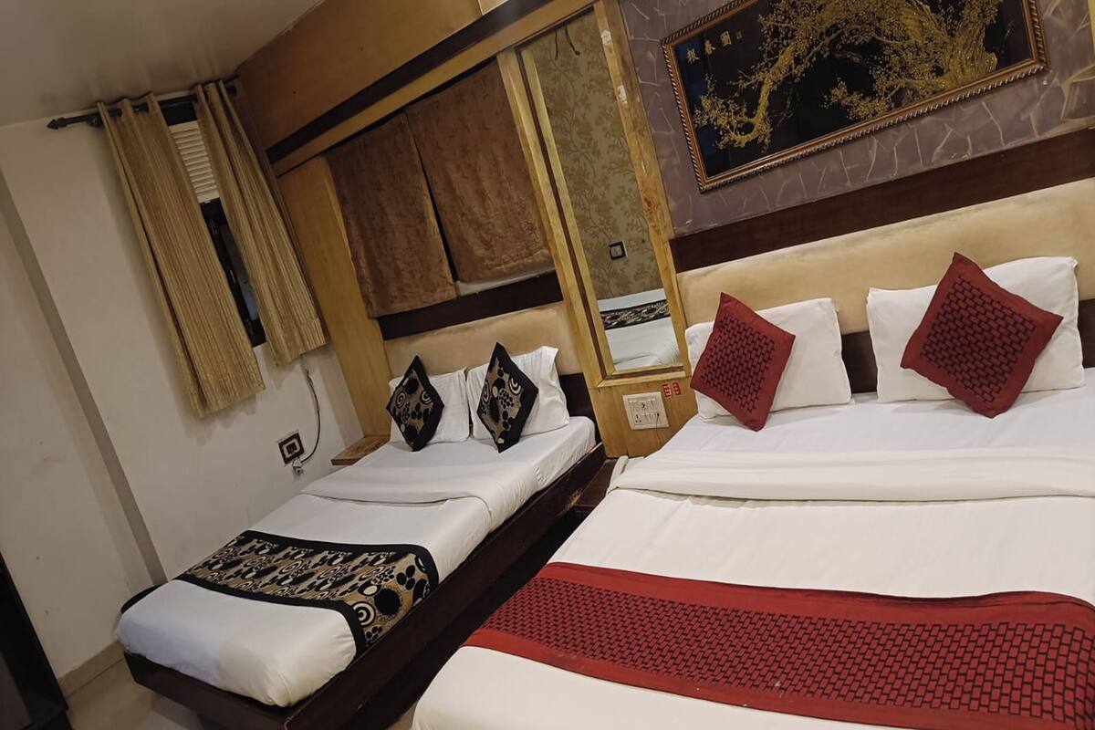 A hotel room with two beds, a wooden headboard, a red and black patterned bedspread, and a wall-mounted painting.
