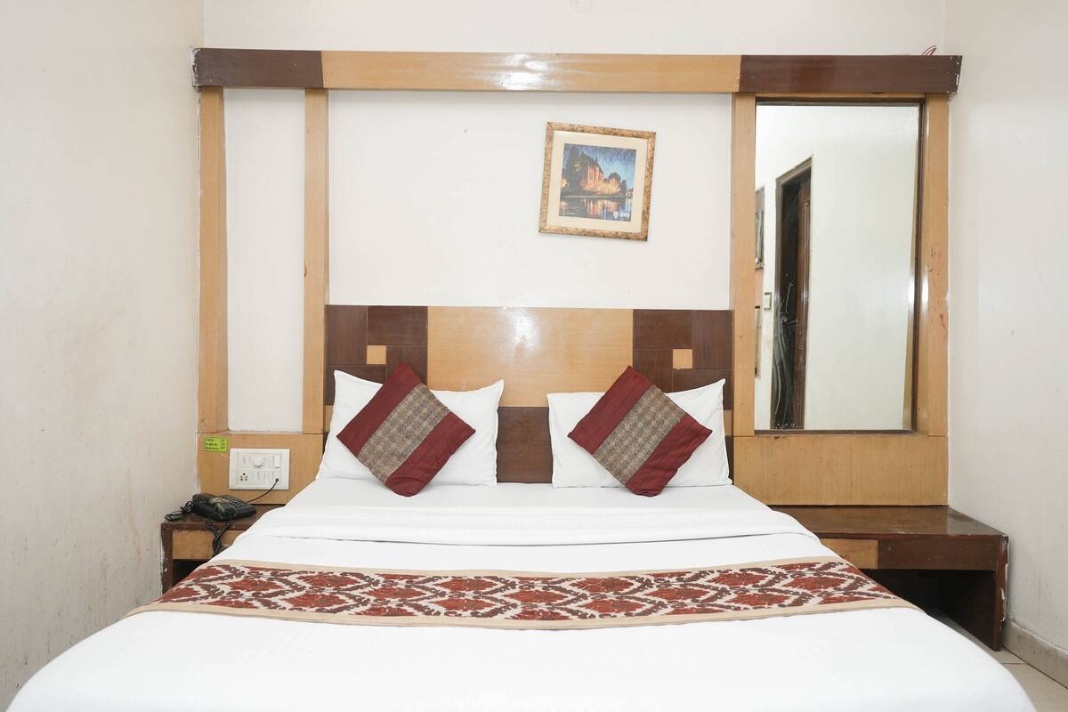 A neatly made bed with a patterned bedspread, a wooden headboard, and a framed picture on the wall.