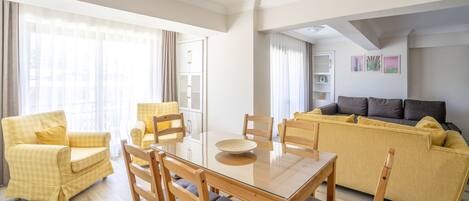 A modern living room with a glass-top dining table, yellow armchairs, and a sofa.