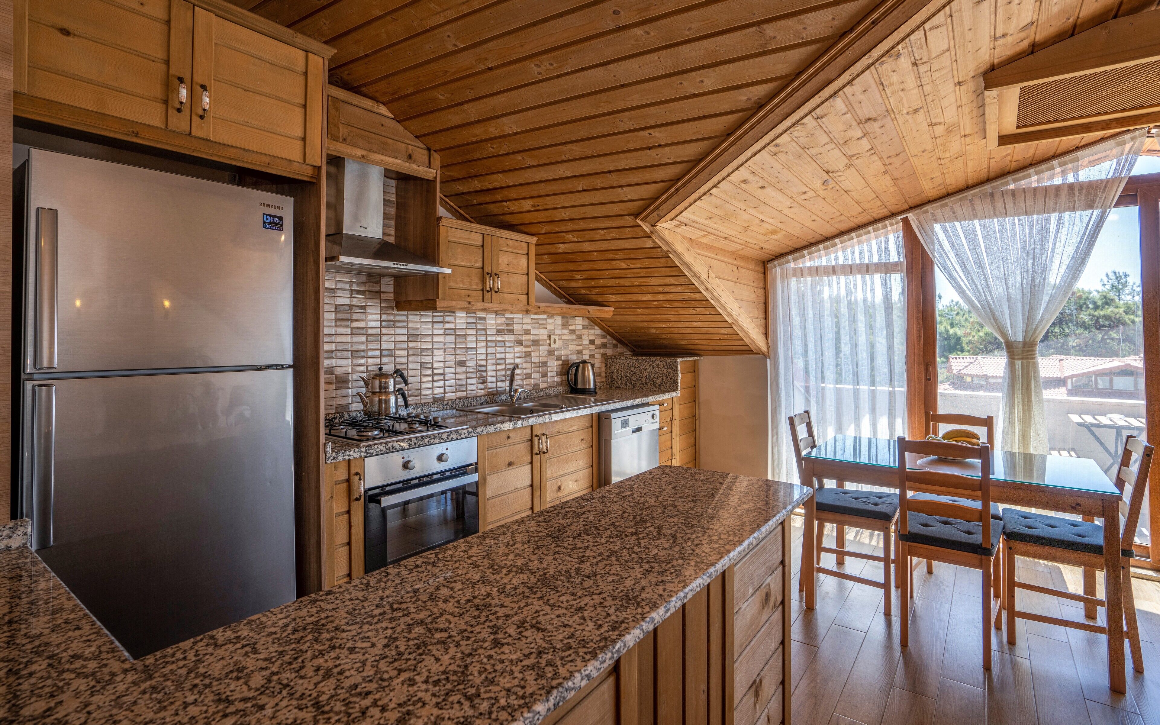 Una cocina con armarios de madera, un refrigerador de acero inoxidable, una estufa y un comedor con mesa y sillas.