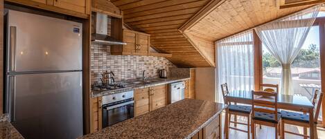 Una cocina con armarios de madera, un refrigerador de acero inoxidable, una estufa y un comedor con mesa y sillas.