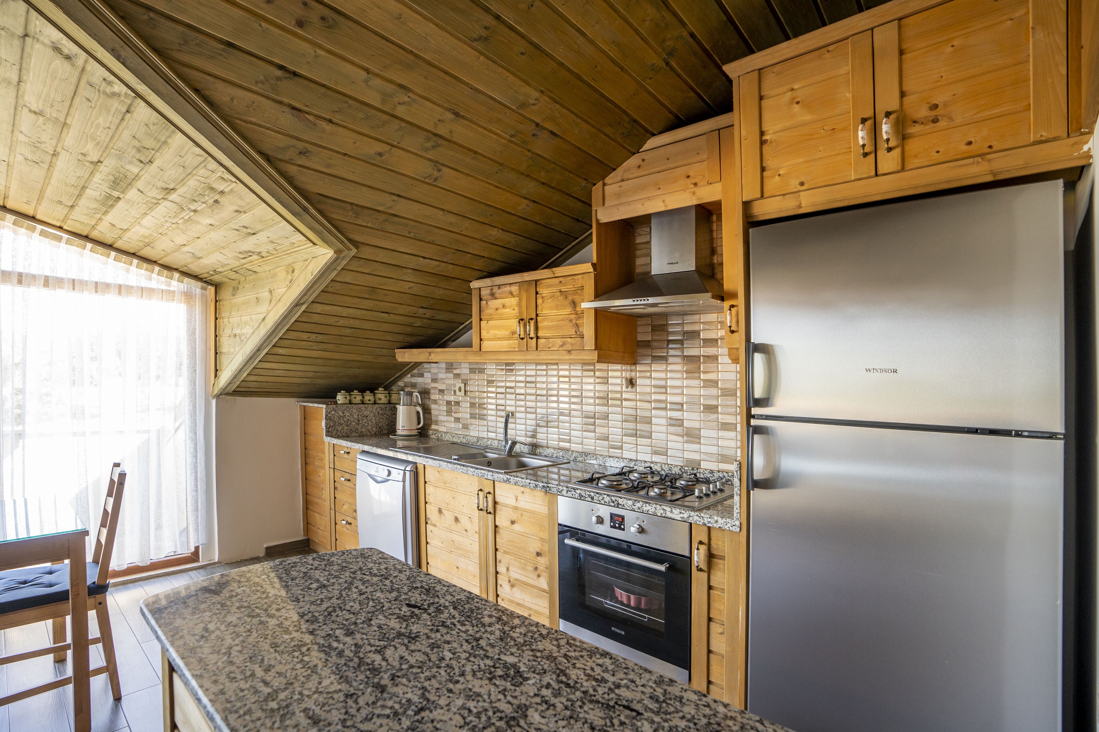 Una cucina con mobili in legno, un frigorifero in acciaio inossidabile, un piano cottura a gas e uno schienale piastrellato.