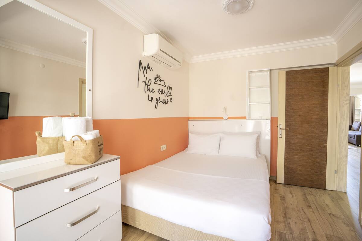 A hotel room with a bed, a dresser, a mirror, an air conditioning unit, and a motivational wall decal.