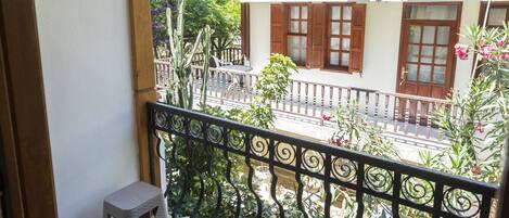 A balcony with two stools, a satellite dish, and a building with wooden shutters in the background.