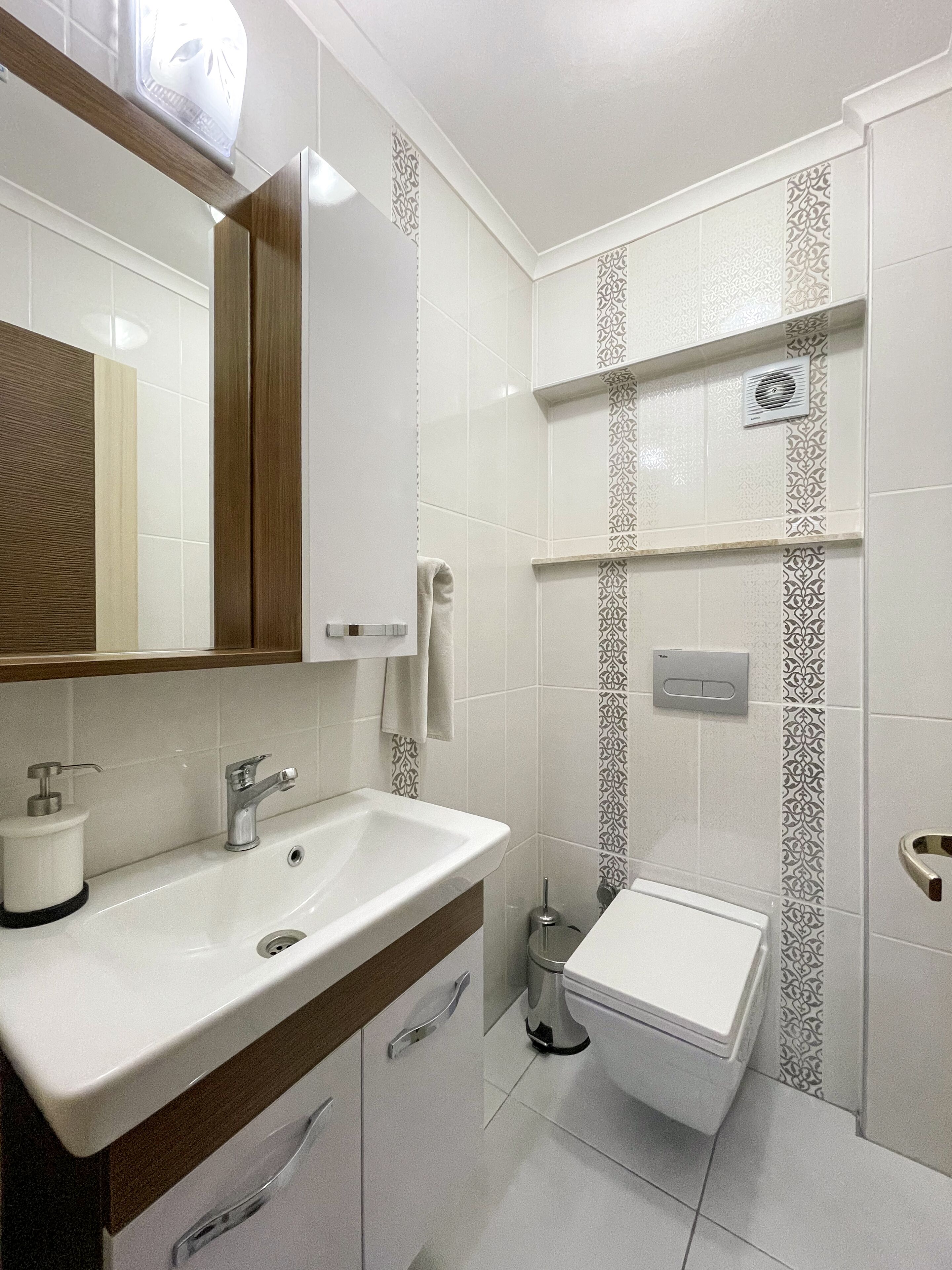 A modern bathroom with a white sink, mirror, and toilet.