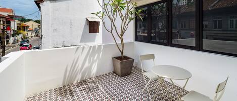 A balcony with a potted plant, a small table, and a chair.