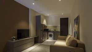 Un salón moderno con televisor de pantalla plana, un sofá, una mesa de centro con una planta y una zona de cocina con lavadora.