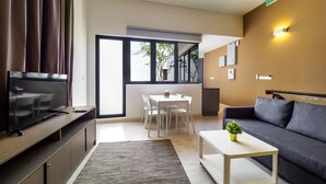 Una sala moderna con una televisión de pantalla plana, un sofá, una mesa de centro y un comedor con una mesa y sillas.