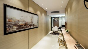 Un moderno vestíbulo de hotel con una gran obra de arte urbana enmarcada, un mostrador de recepción y un área de estar con una mesa y sillas de madera.