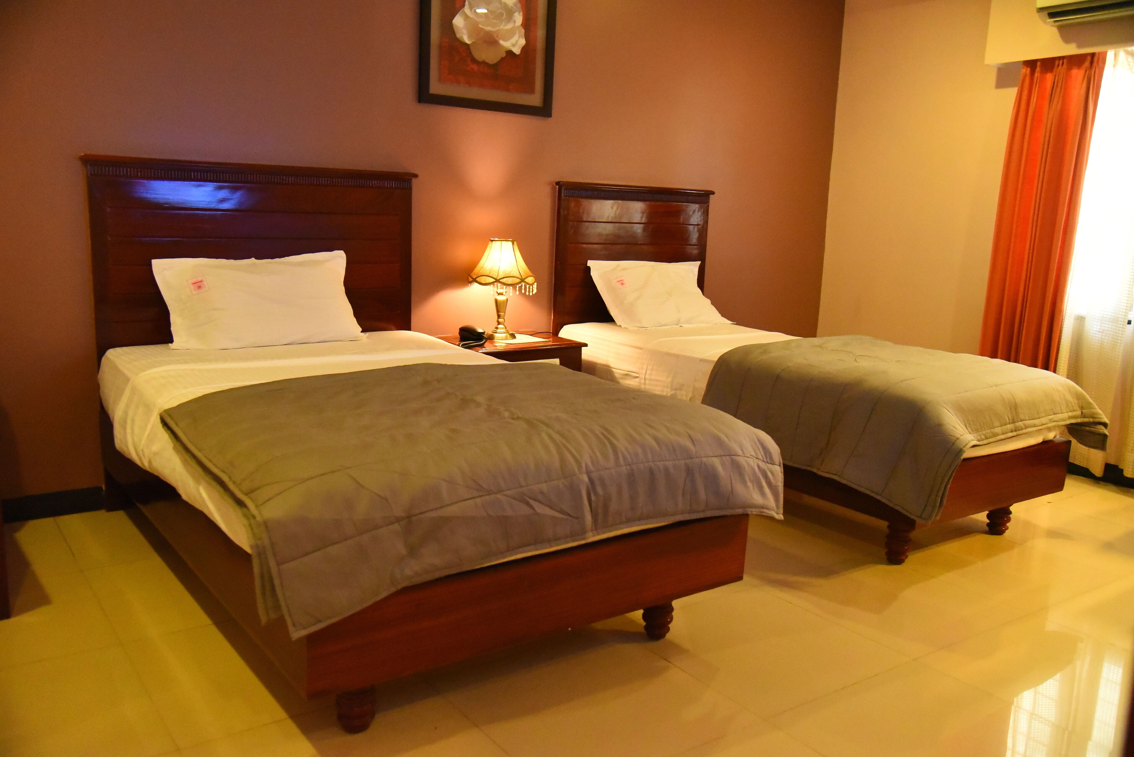A hotel room with two beds, a nightstand with a lamp, and a framed picture on the wall.