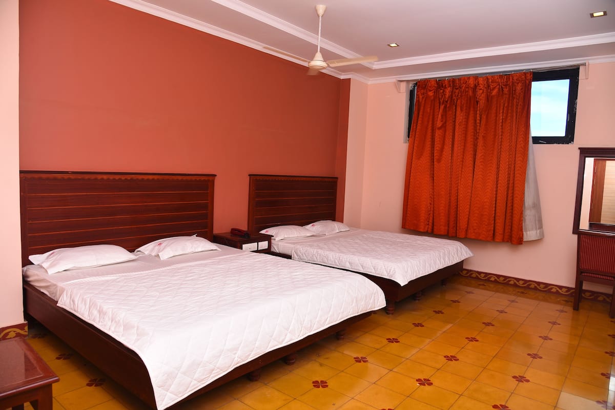 Une chambre d’hôtel avec deux lits simples, une tête de lit en bois, un ventilateur de plafond et une fenêtre avec des rideaux orange.