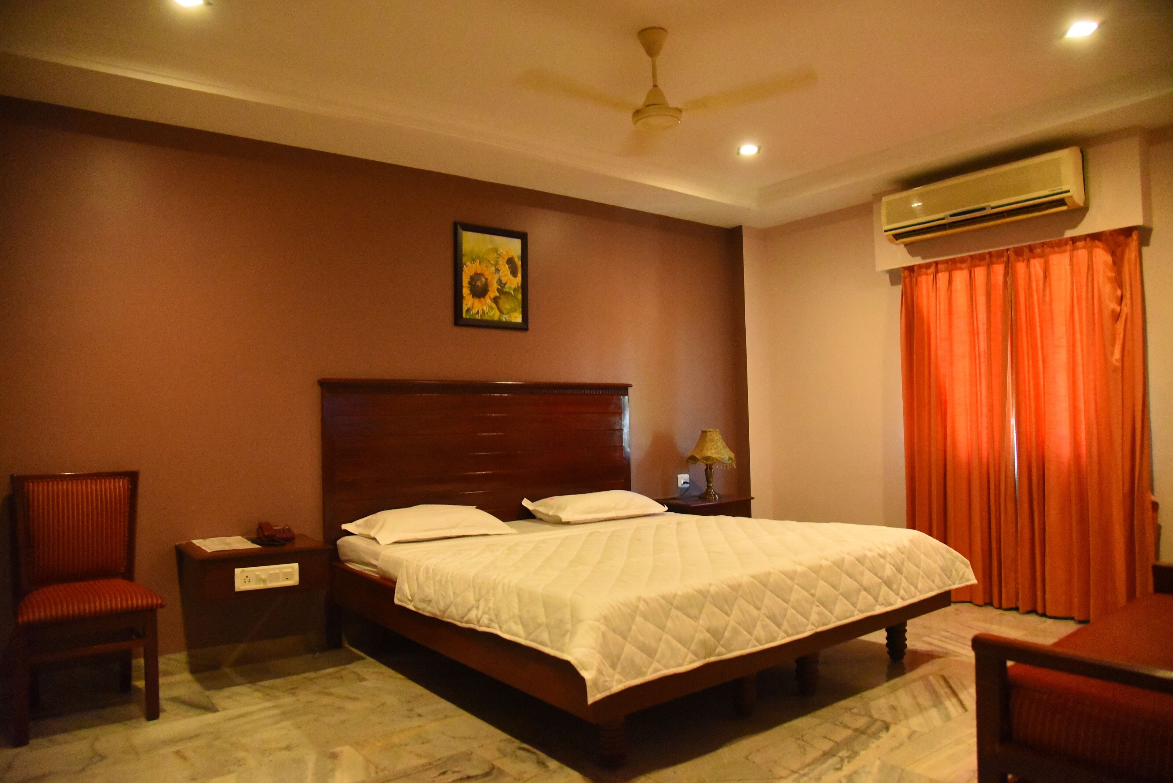 A bedroom with a wooden bed, a nightstand, a chair, an air conditioning unit, and a ceiling fan.