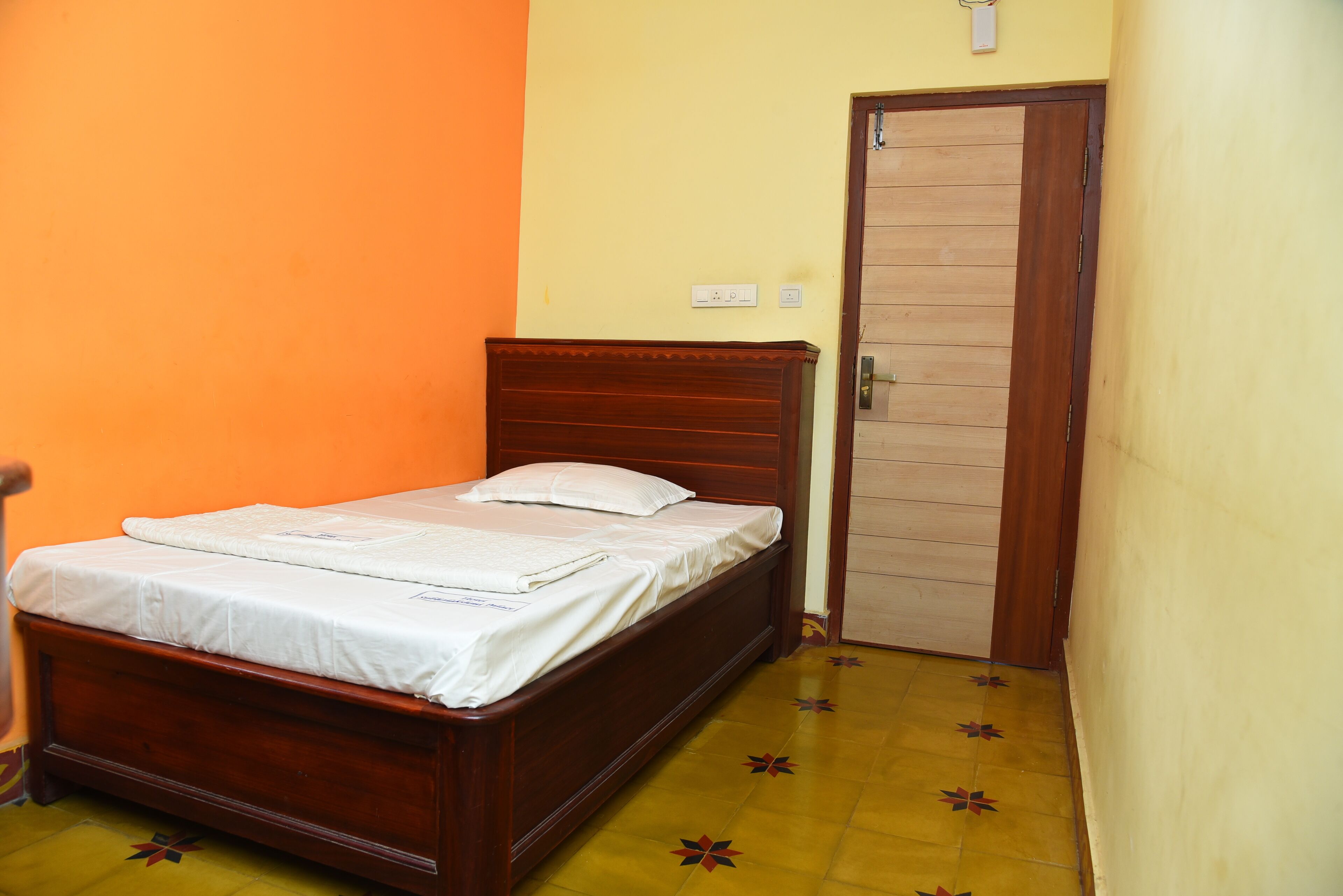 A single bed with a wooden headboard in a room with orange and yellow walls and a door with a wooden panel.