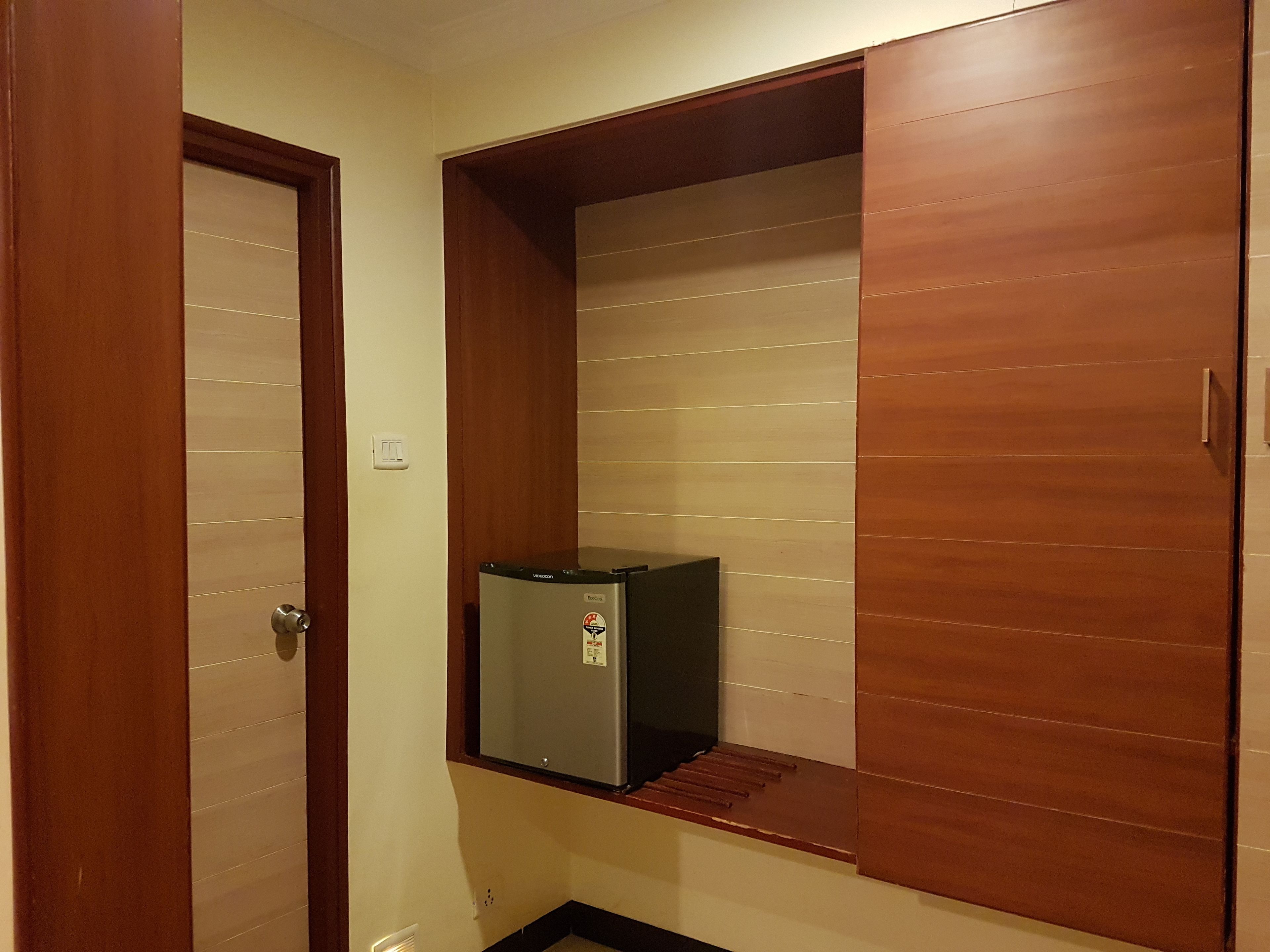 A compact room with a built-in refrigerator, a door, and a small shelf.