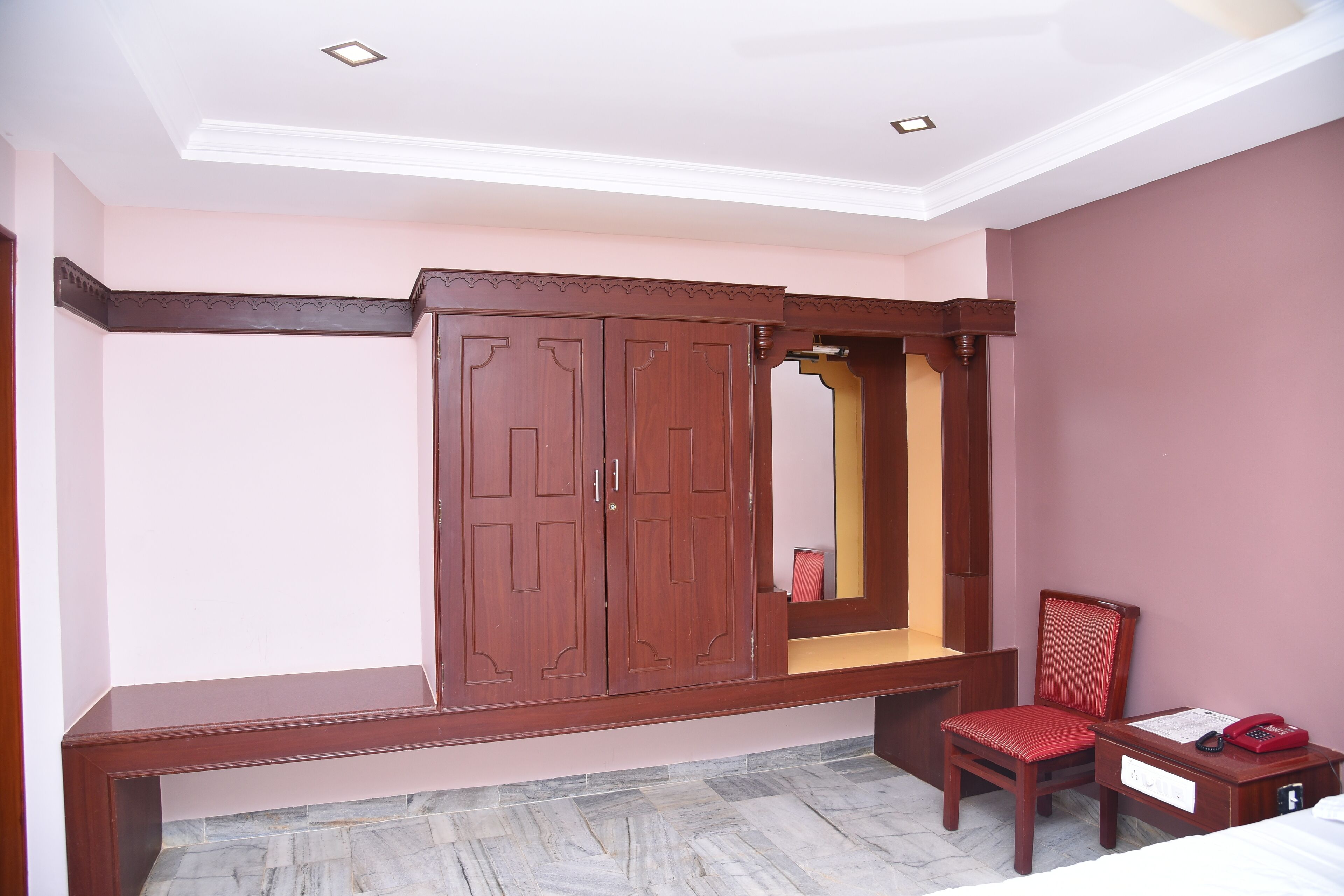 A bedroom with a wardrobe, a chair, a bedside table, and a bed.