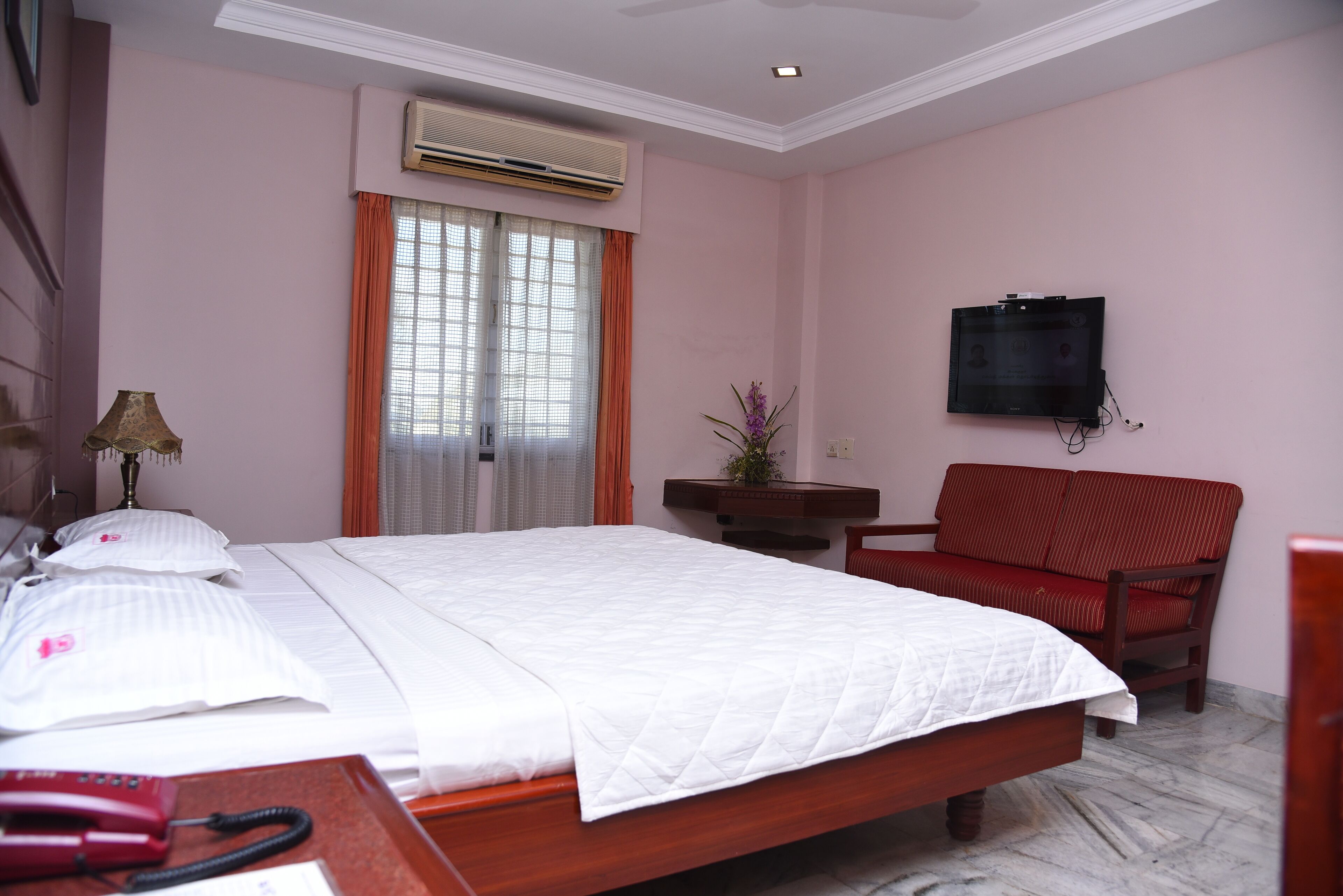 A hotel room with a bed, a chair, a desk with a telephone, and a television.