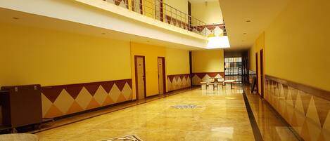 A multi-level hotel corridor with a polished marble floor, geometric wall patterns, and a mezzanine with a railing.