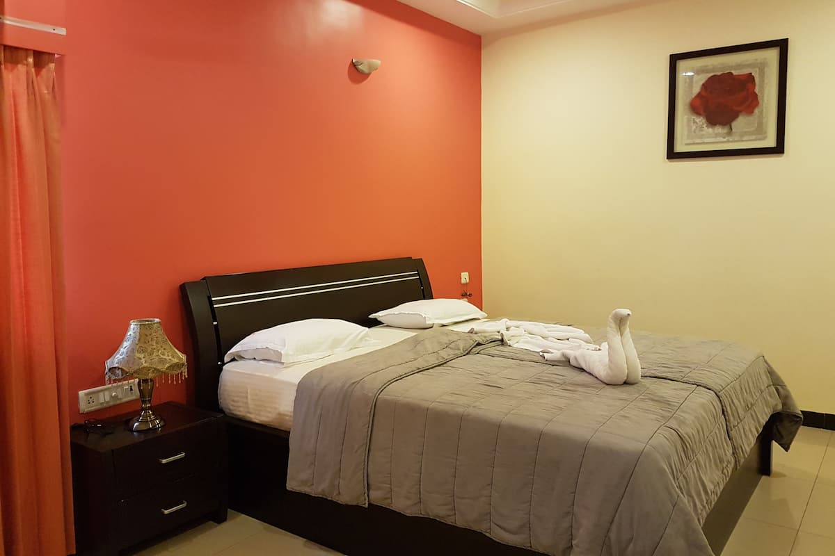 Un lit bien fait, avec une couvre-lit grise et des oreillers blancs, une table de chevet avec une lampe et un tableau encadré au mur.