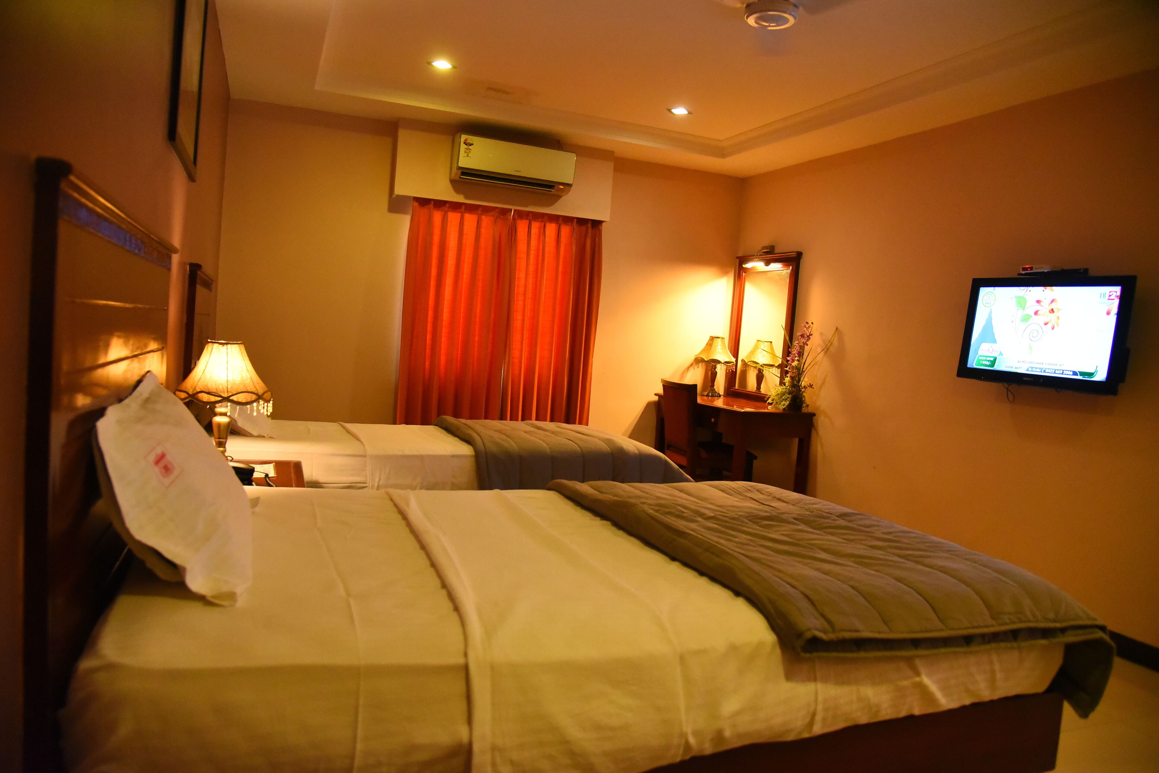 A hotel room with two beds, a television, an air conditioner, and a lamp.