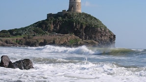 Una fortificación costera con una torre, rodeada por olas y afloramientos rocosos.
