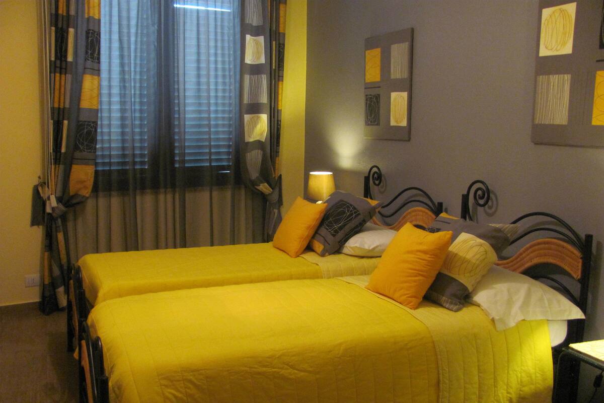 A room with two beds, each with yellow bedding, a headboard with a unique design, and a wall with artwork.