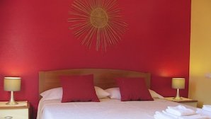 Una cama bien hecha con dos almohadas, una lámpara de noche a cada lado y un sol radiante decorativo en la pared.