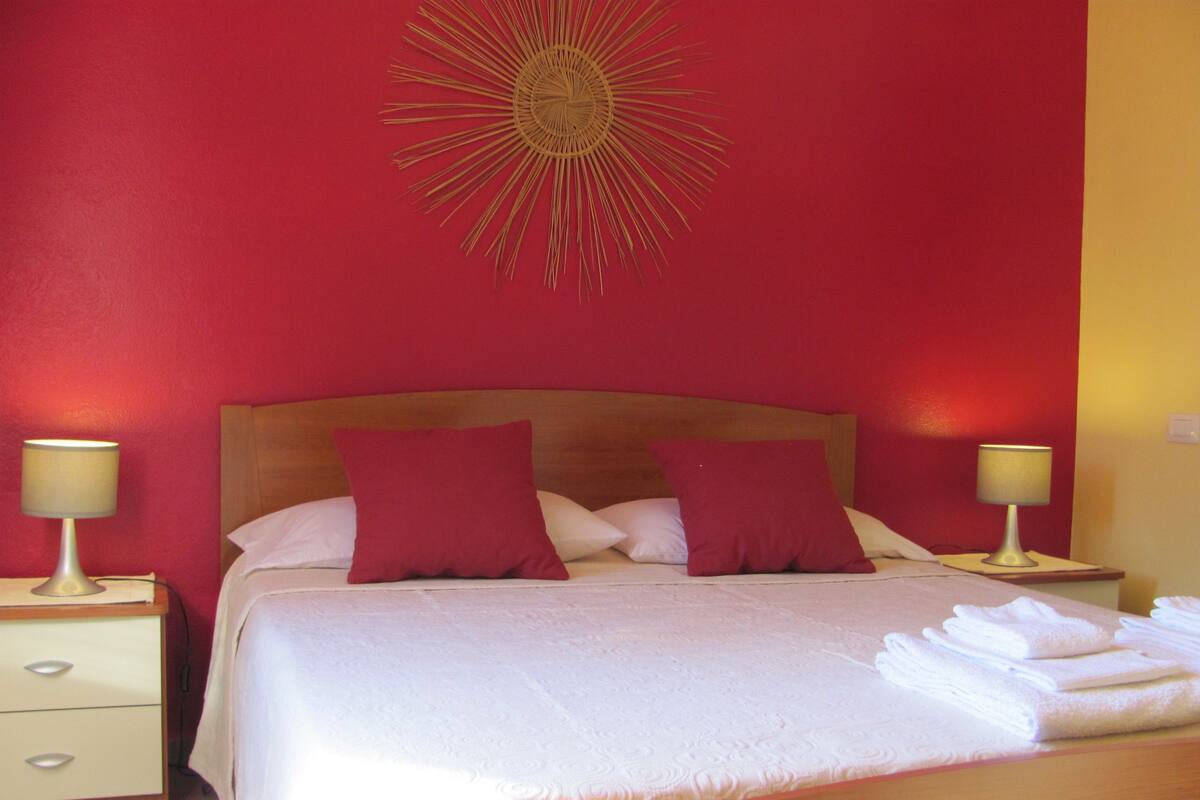 A neatly made bed with two pillows, a bedside lamp on each side, and a decorative sunburst on the wall.