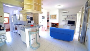 A modern kitchen with white cabinets, a blue sofa, and a dining area with a pink tablecloth. - Portorosa Residence (Furnari)