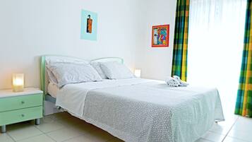 A neatly made bed with a white and gray patterned bedspread, a green nightstand with a lamp, and two wall art pieces.