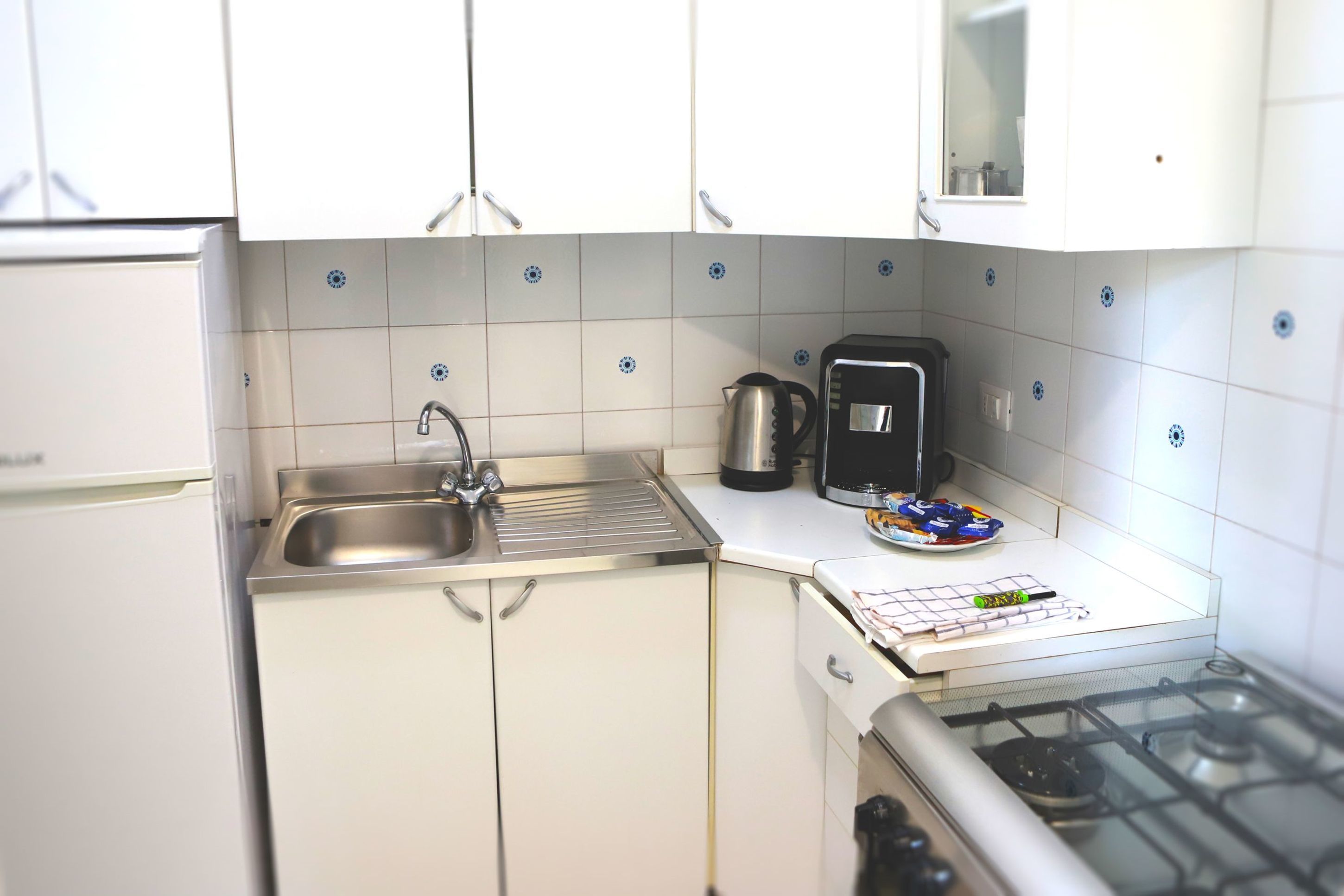 A compact kitchen with white cabinets, a stainless steel sink, a coffee maker, and a gas stove.