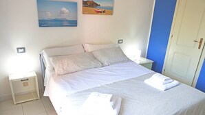 A neatly made bed with white linens, a bedside table with a lamp, and a door to the right. - Portorosa Residence (Furnari)