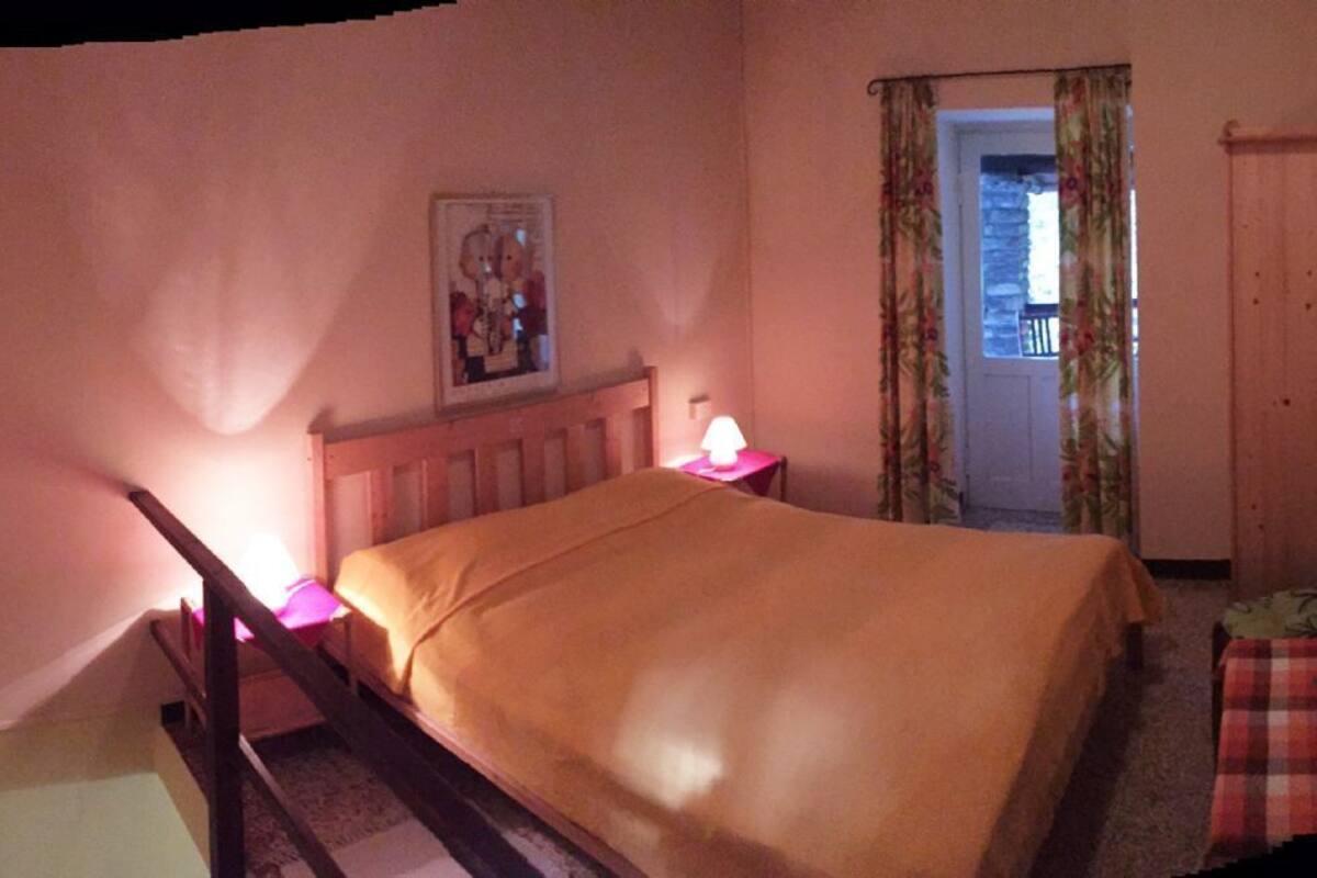 Une chambre à coucher avec un lit, une table de chevet, une lampe, une porte avec des rideaux et un tableau encadré au mur.