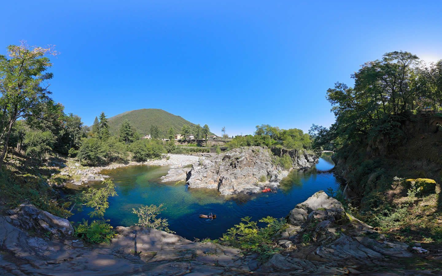 Un paisaje natural con un lago azul cristalino, terreno rocoso y una montaña al fondo.