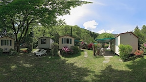 A row of mobile homes with a grassy yard and a pathway leading to a covered area. - Camping Valle Romantica (Cannobio)