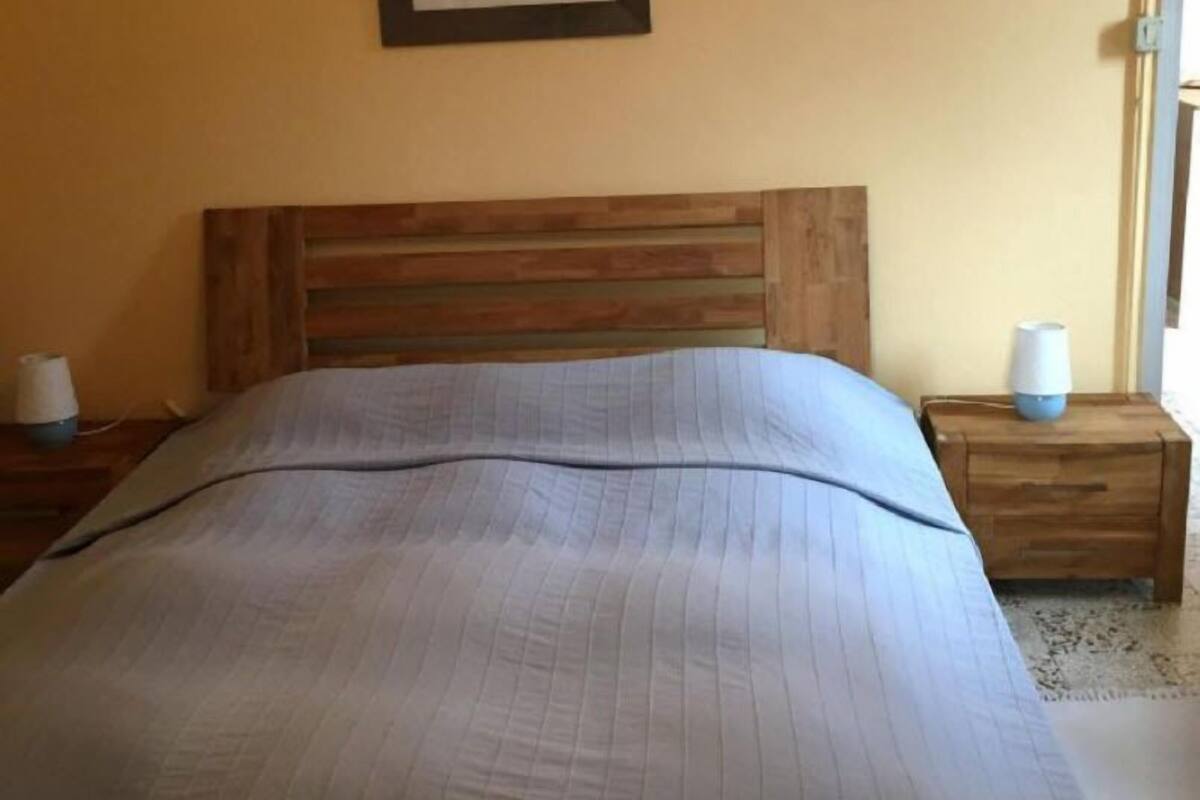 Une chambre avec une tête de lit en bois, un lit recouvert d’une couverture à rayures, une table de chevet avec une lampe et un tableau encadré accroché au mur.